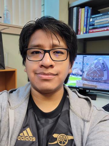 image of man head and shoulders in an office, in front of books on bookcase 