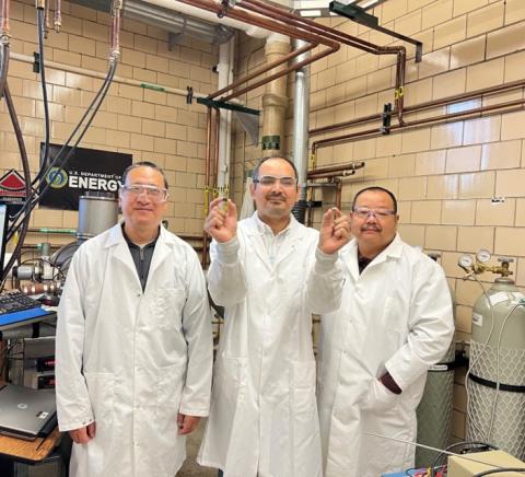image of three people standing in a research laboratory: Rakesh Chaudhary (center) from AML holding two magnets he fabricated at Ames National Laboratory. Baozhi Cui (left), and Jun Cui (right), mentors from Ames.