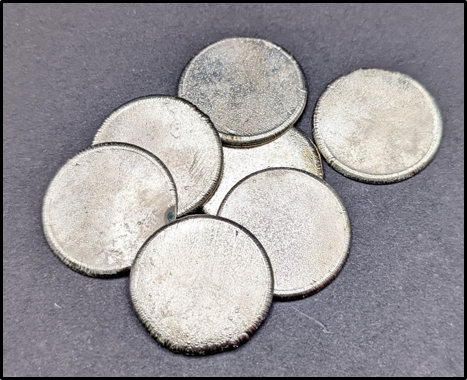 image of seven silver pieces of metal that are Ni/Co alloy rounds, ~3 cm diameter, 99.5% purity.