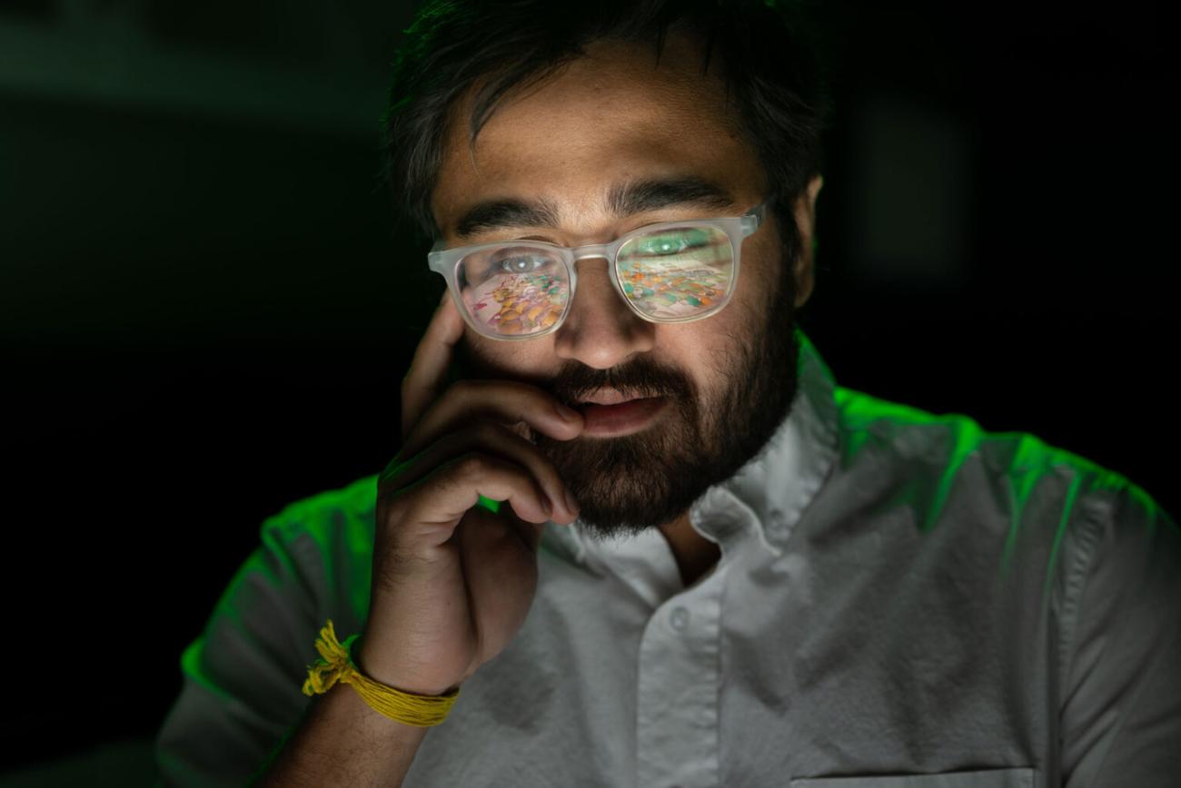 image of man head and shoulders, with green light reflected in eyeglasses