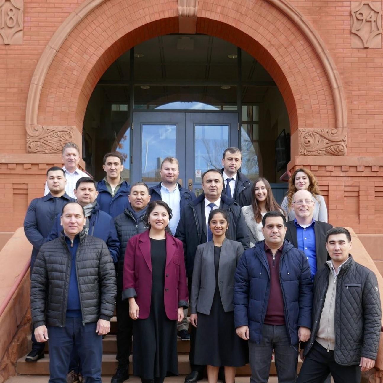 image of group of about a dozen people standing on stairs by a red brick building