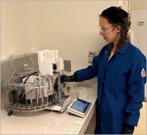 person standing by research equipment: Aubrey Lemer using CMI high-throughput auto-balance to prepare leaching samples.