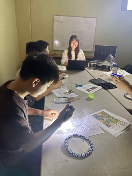 several people seated at a table with nearest one shining a light on phosphor paper